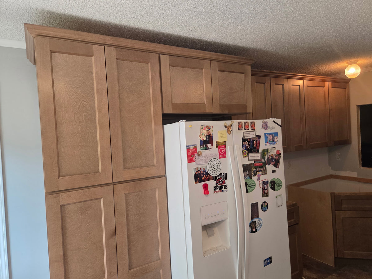 Floor to ceiling pantry cabinets in light stained wood with refrigerator surround and crown molding